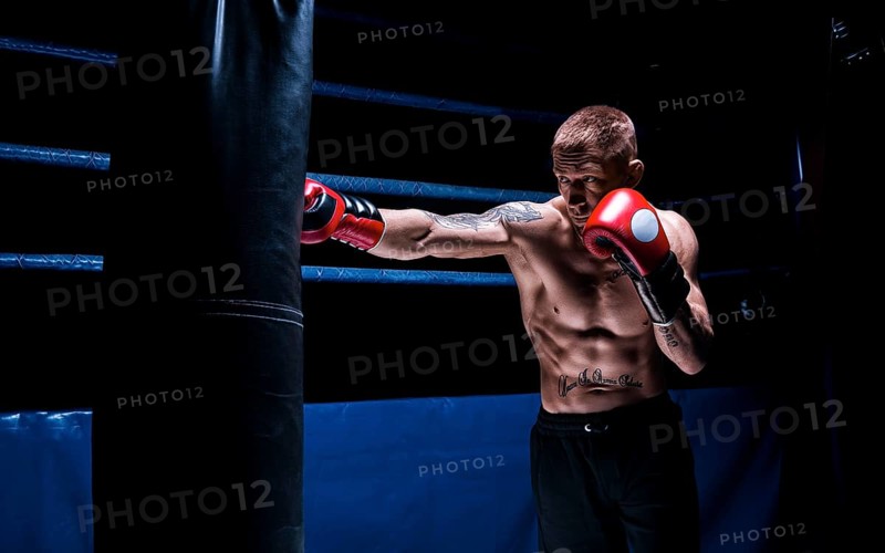 Professional boxer hits the bag against the background of the ring. Side view. The concept of sport and classic boxing.