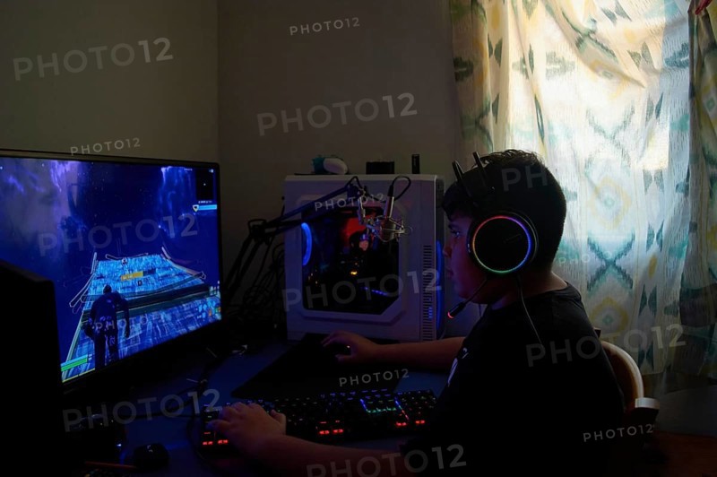 Side View of teenage gamer boy playing video games online on computer in dark room