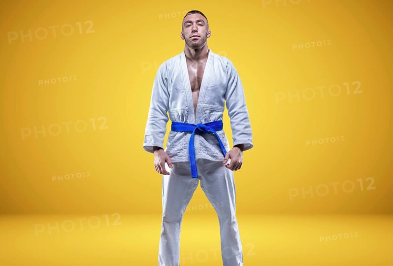 Strong man in a kimono with a blue belt. Yellow background. Martial arts concept.