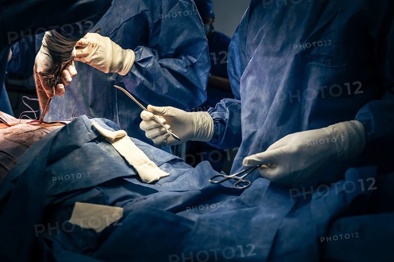 Surgeons and instrumental assistant are performing a surgical operation in the emergency room of a hospital. An assistant hands scissors and instruments to the surgeons during the operation