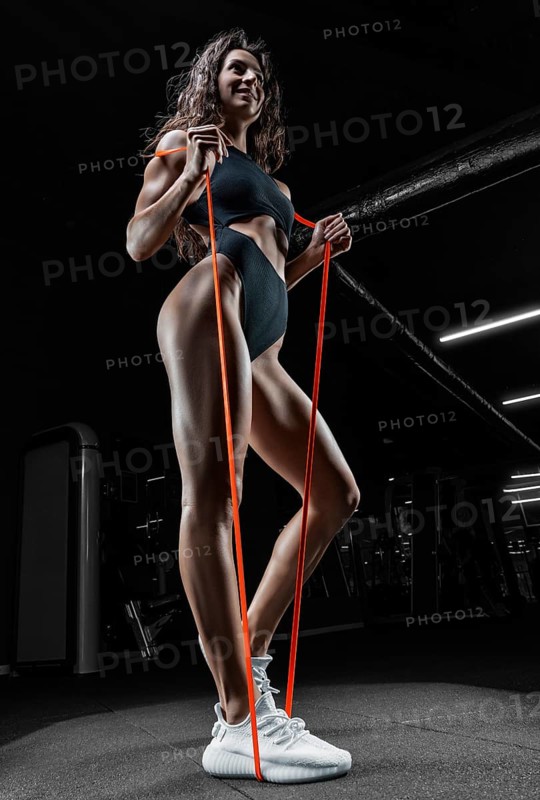 Tall athletic woman posing with gymnastic elastic bands in the gym. Fitness and bodybuilding concept.