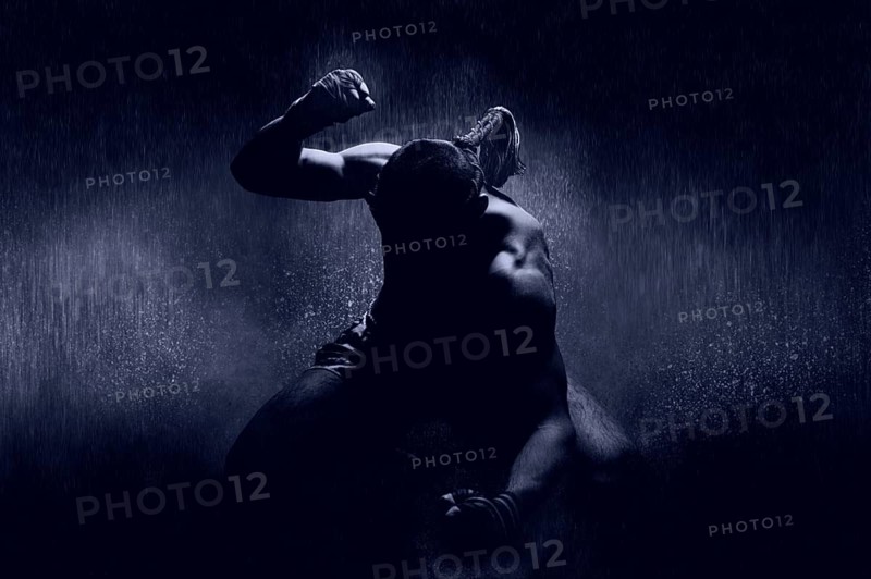Thai boxer in the rain and under a blue spotlight. Mongkhon. The concept of victory in competitions