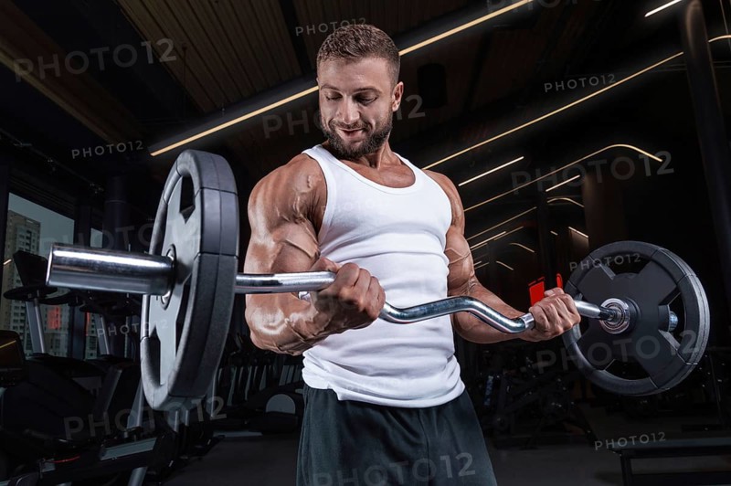 Handsome young man working out with a barbell in the gym. Biceps pumping. Fitness and bodybuilding concept.