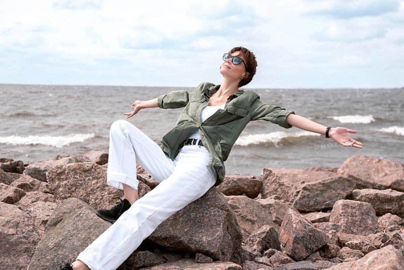 Portrait of a stylish woman sitting on stones in the bay. Windy weather. Happiness