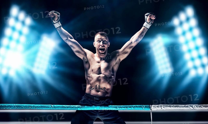 Kickboxer posing in the ring. The athlete climbed the ropes and took a victorious position against the background of spotlights. The concept of mma