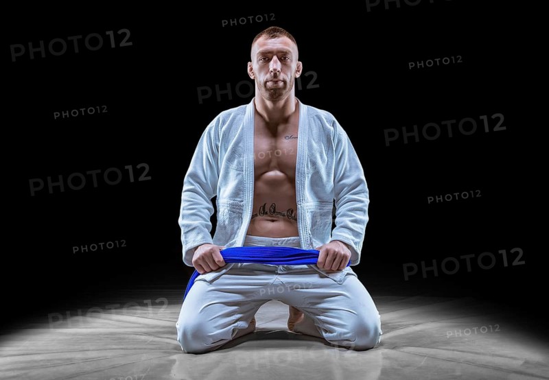 Professional athlete sits in the gym in a kimono with a blue belt. Concept of karate