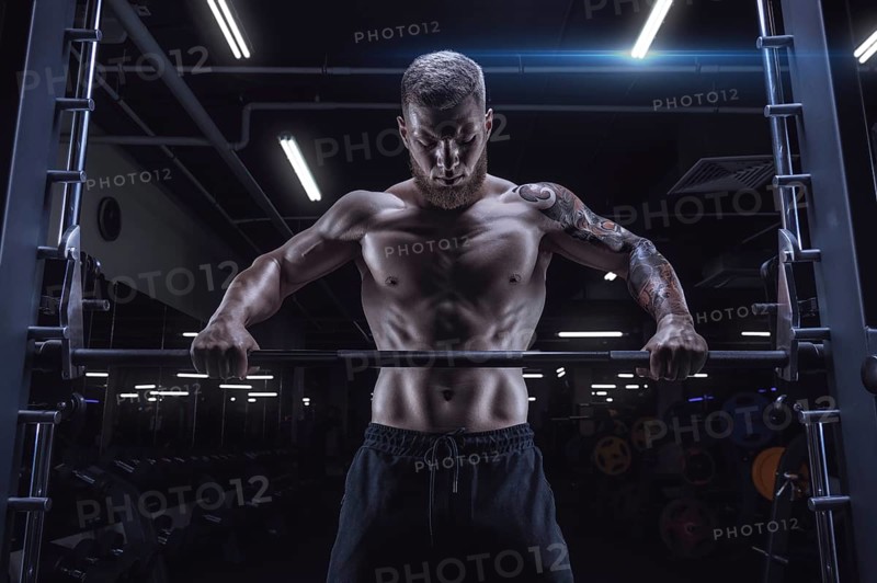 Portrait of an athlete standing in front of a barbell in the gym. Bodybuilding and fitness concept.