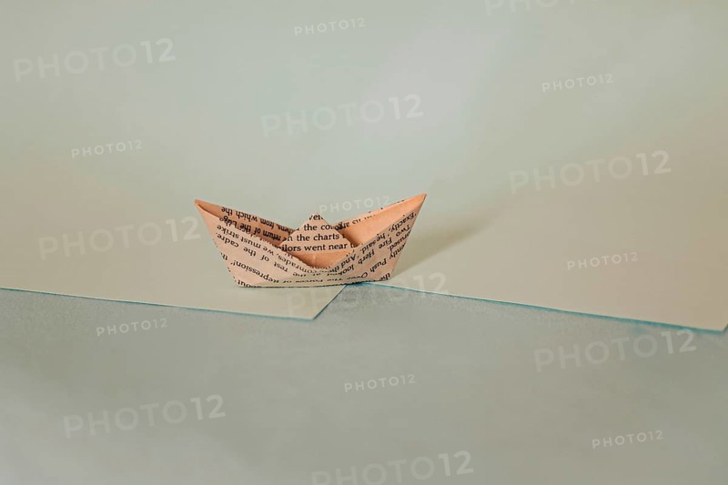 A simple origami paper boat on a diagonal split background with blue hues