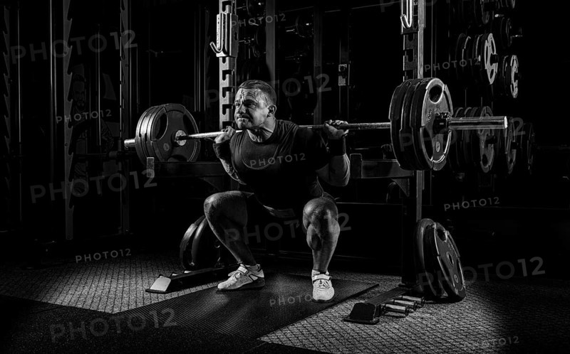 The weightlifter is getting ready to stand with a heavy barbell. Is at the bottom point