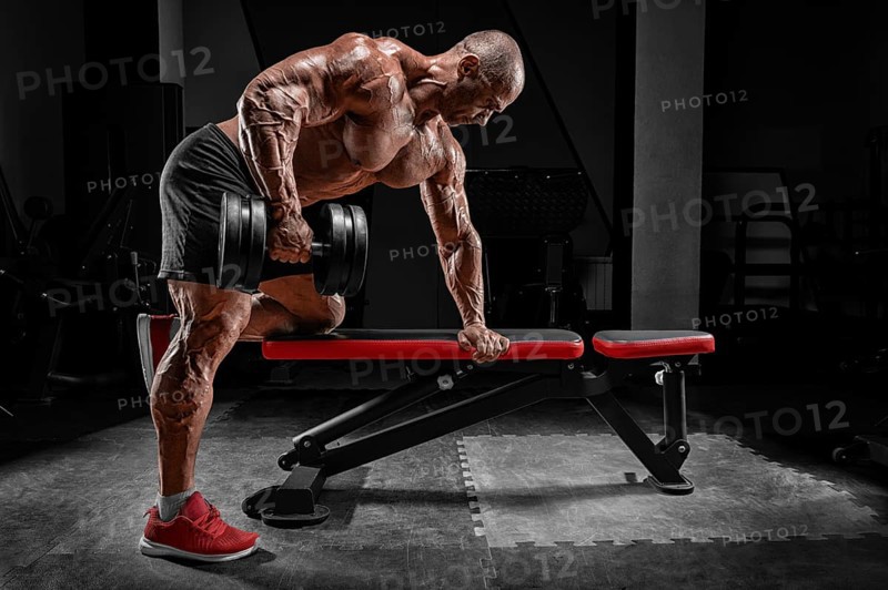 Muscular man pulls a dumbbell towards his stomach. Bodybuilding and powerlifting concept.