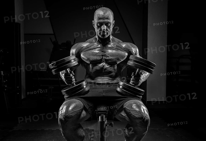 Muscular man sits on a bench with dumbbells. Bodybuilding and powerlifting concept.