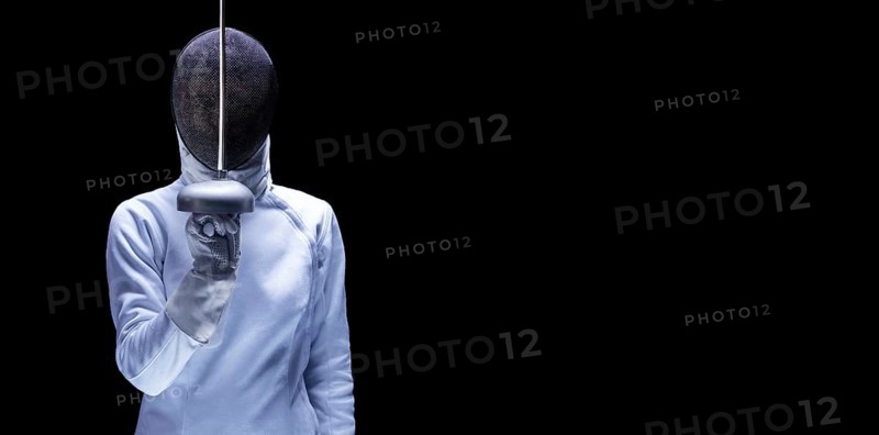 Charming girl dressed as a fencer posing with a mask and a sword. The concept of fencing.