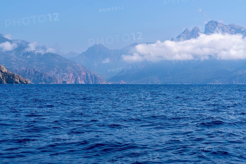 A calm seascape with mountains in the background and clouds in the sky