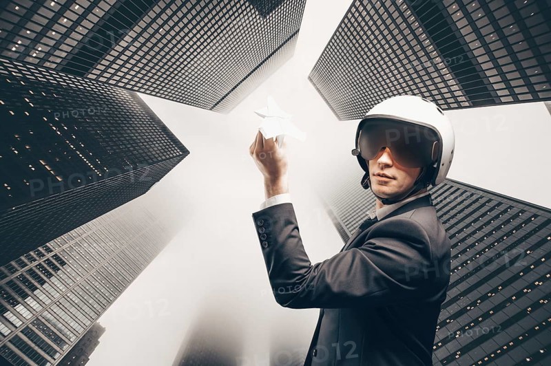 Portrait of a man in a suit and helmet. He launches a paper airplane up to the roofs of the skyscrapers of the financial district. Business concept.
