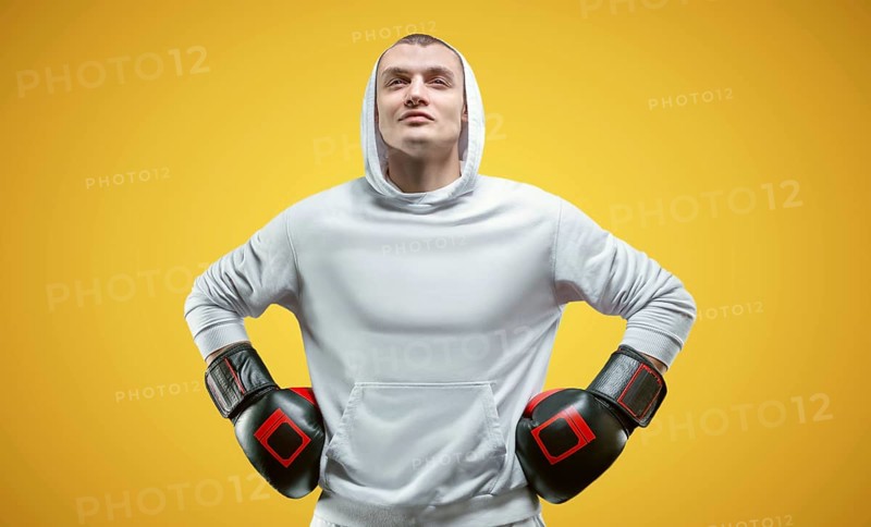 Male trainer posing in the studio with boxing gloves. White hoodie. Mixed martial arts concept. High image quality