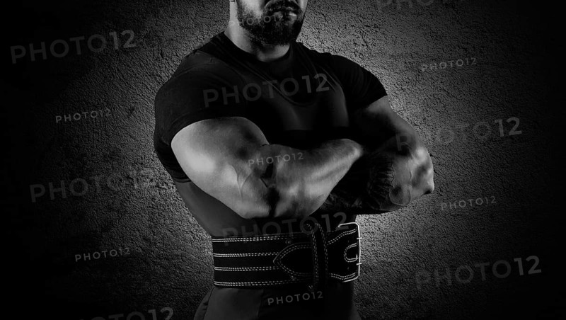 The weightlifter stands in a menacing pose with crossed huge arms and looks at the camera
