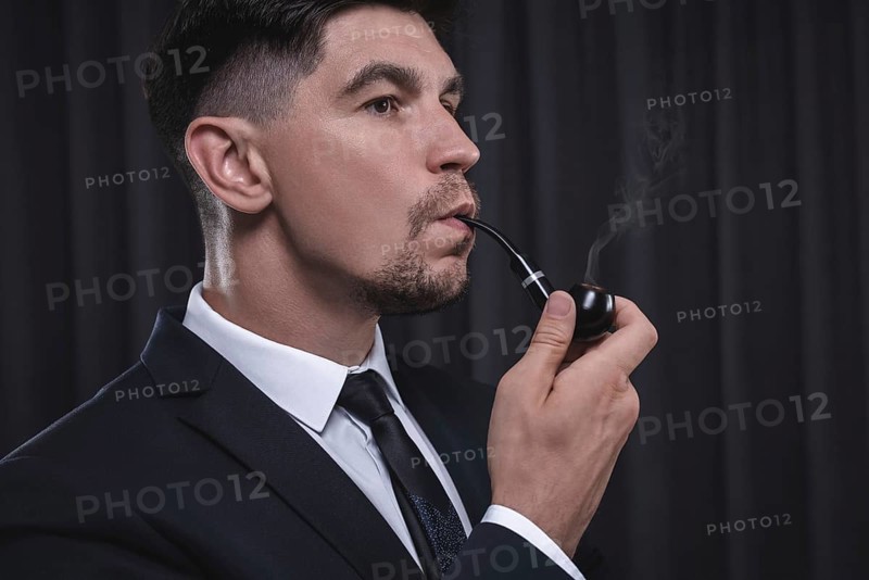 Image of an elegant man in a suit smoking a pipe. Business success concept.