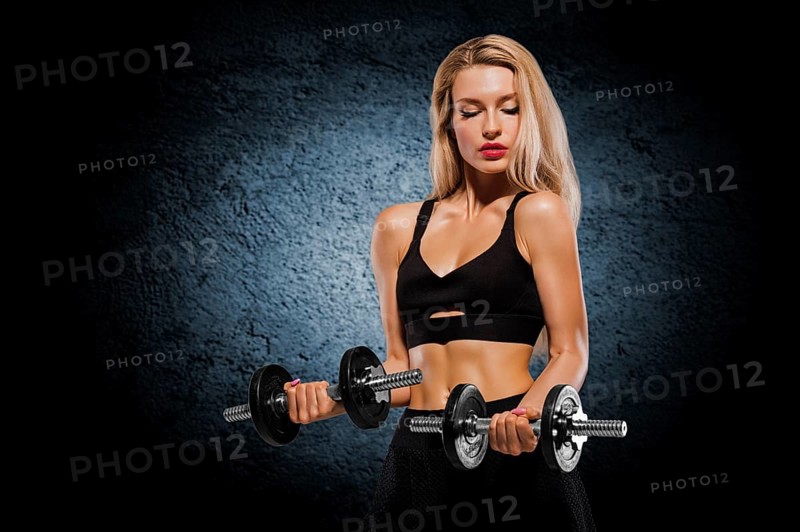 Sportive girl with an ideal figure posing in the studio with dumbbells in her hands.