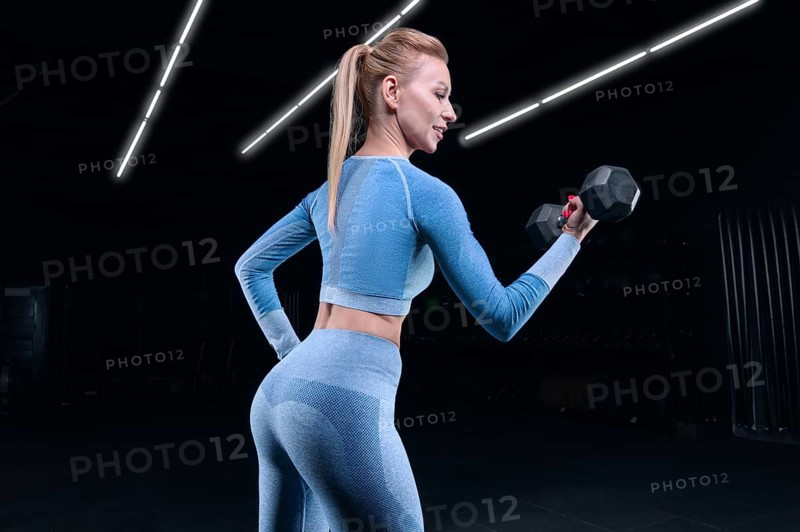 Charming sportswoman posing in the gym with dumbbells. The concept of bodybuilding