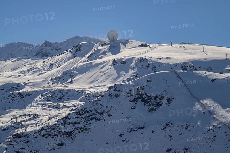 Snow-covered mountain under a clear blue sky with a radar antenna at the peak