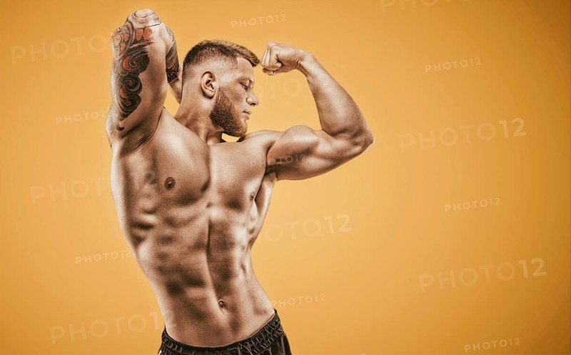 Young muscular guy with nice abs posing on an orange background. Fitness and nutrition concept.