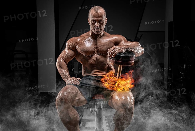 Muscular man sits on a bench with dumbbells burning. Bodybuilding and powerlifting concept.
