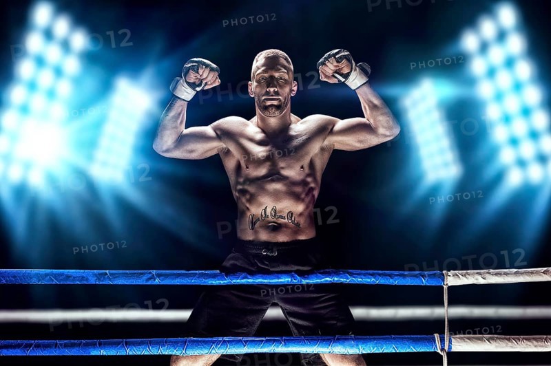 Kickboxer posing in the ring. The athlete climbed the ropes and took a victorious position against the background of spotlights. The concept of mma