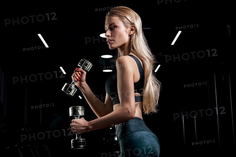 Charming sportswoman posing in the gym with dumbbells. The concept of bodybuilding