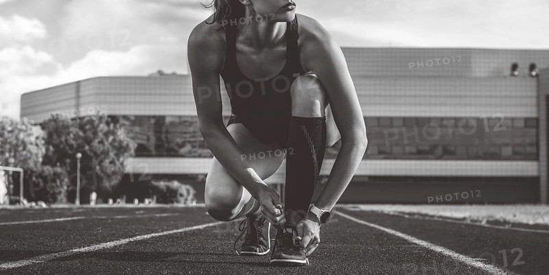 Image of a young female runner laces her shoes on a stadium track. Sports concept.