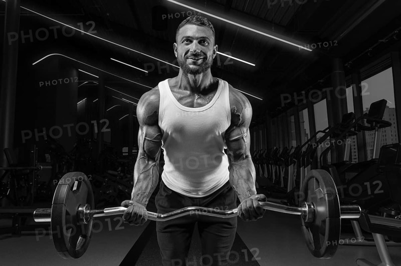 Handsome young man working out with a barbell in the gym. Biceps pumping. Fitness and bodybuilding concept.