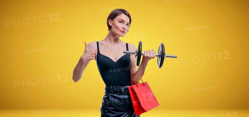 Beautiful slender woman posing in the studio with a dumbbell and gift bags. Gift concept. Gym membership. Ok sign.