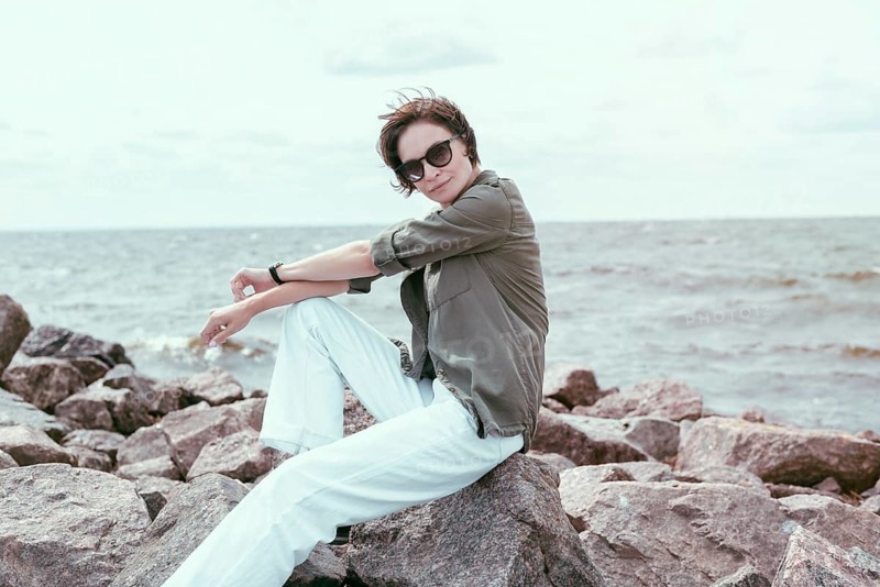 Portrait of a stylish woman sitting on stones in the bay. Windy weather. Happiness