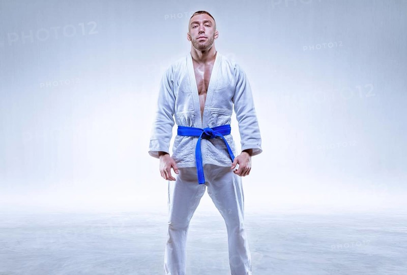 Athlete in a kimono with a blue belt stands on a light background. The concept of karate and judo.