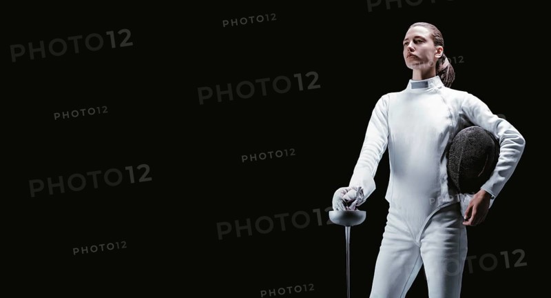 Charming girl dressed as a fencer posing with a mask and a sword. The concept of fencing.