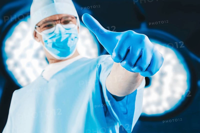 The doctor against the background of surgical lamps shows a raised finger. Medicine concept.
