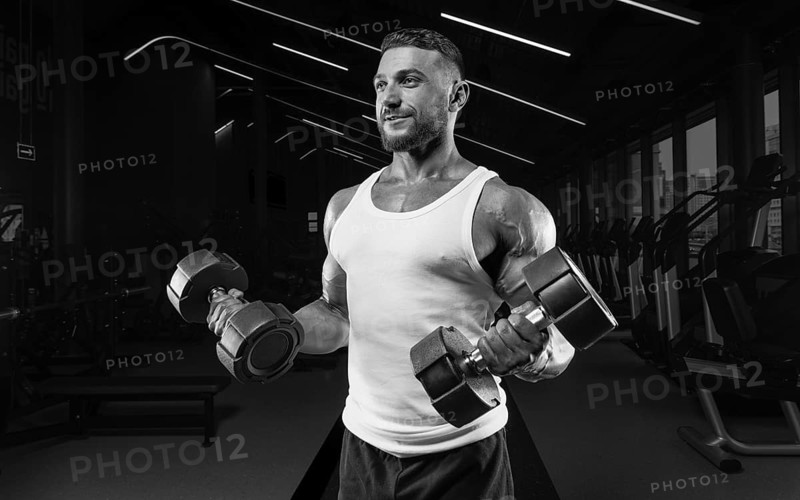 Muscular man in a white t-shirt works out in the gym with dumbbells. Biceps pumping. Fitness and bodybuilding concept.