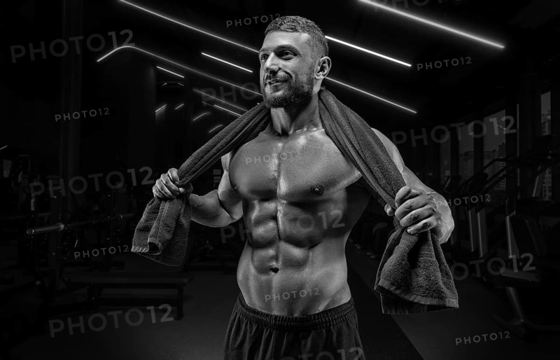 Muscular man posing in the gym with a towel on his shoulders. Fitness concept.