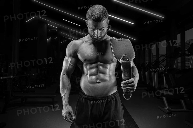Portrait of a muscular guy with a naked torso and abs. Gym. Athletic chain belt. Fitness concept
