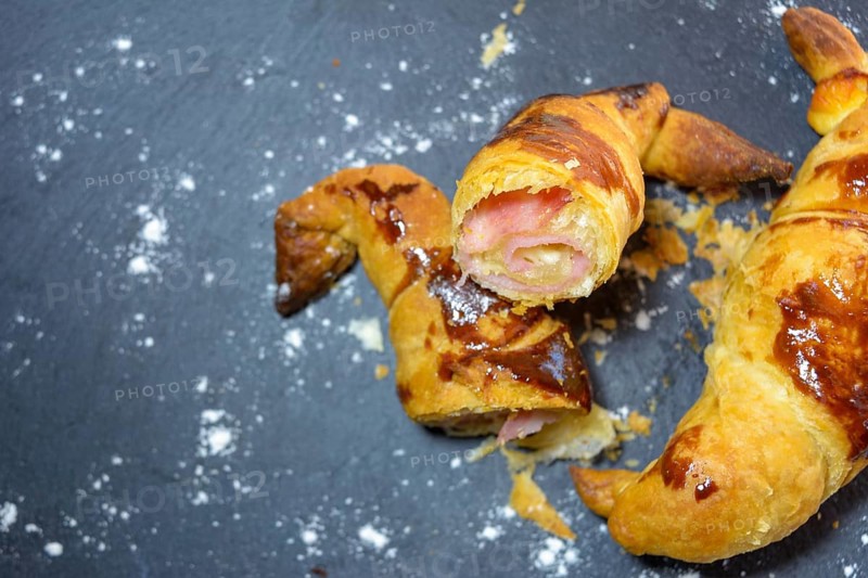 Sliced baked pastry with ham and cheese on a dark background