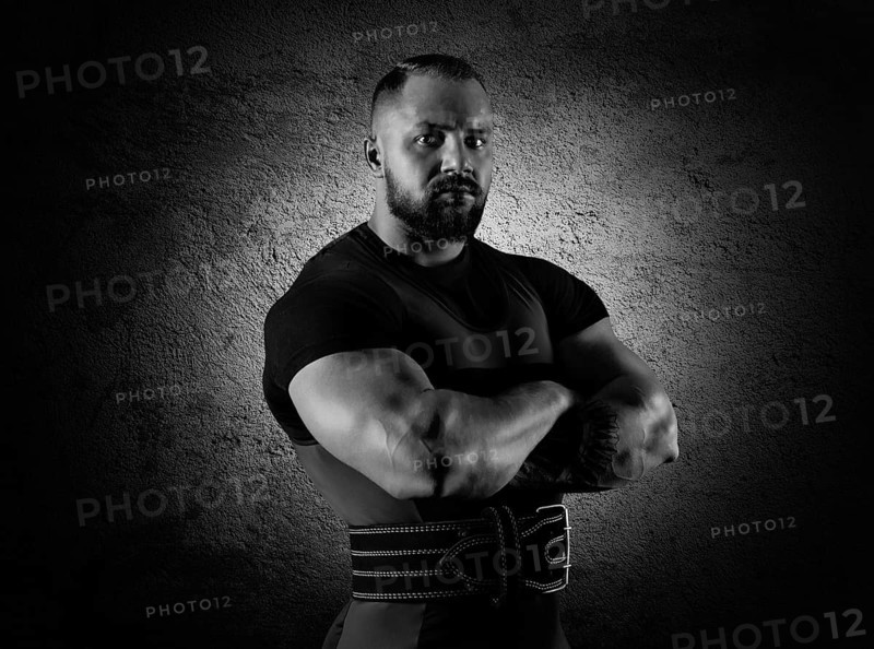 The weightlifter stands in a menacing pose with crossed huge arms and looks at the camera