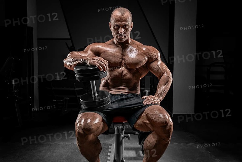 Muscular man sits on a bench with dumbbells. Bodybuilding and powerlifting concept.