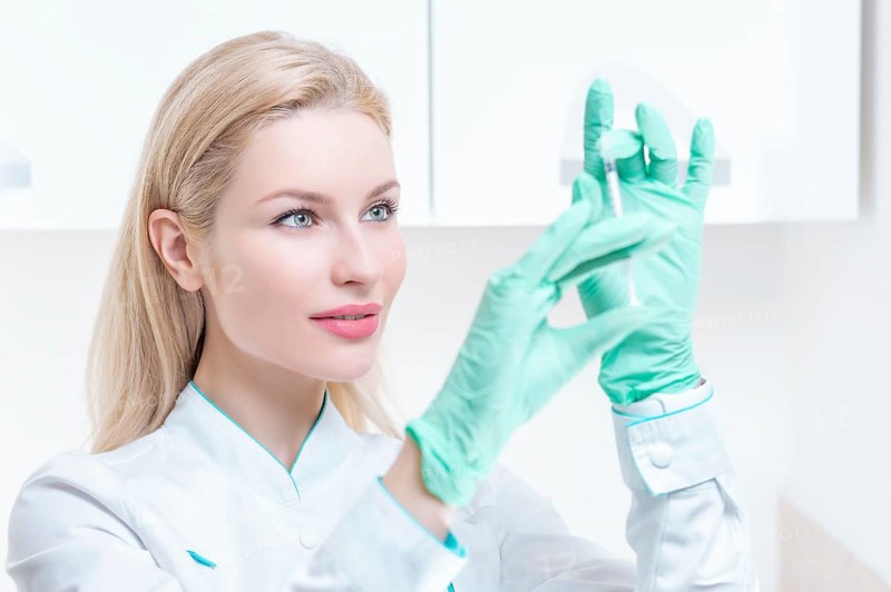 Portrait of a blonde girl in a medical gown with a syringe in her hands. Medical center advertisement.