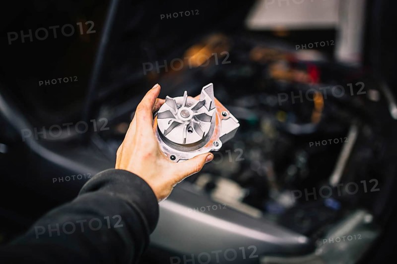 Automotive water pump of the engine cooling system in the hands of an auto mechanic