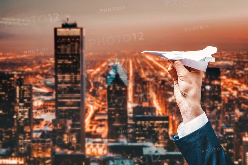 Image of a man's hand in a suit. He launches a paper airplane from the roof of a skyscraper. Business concept.