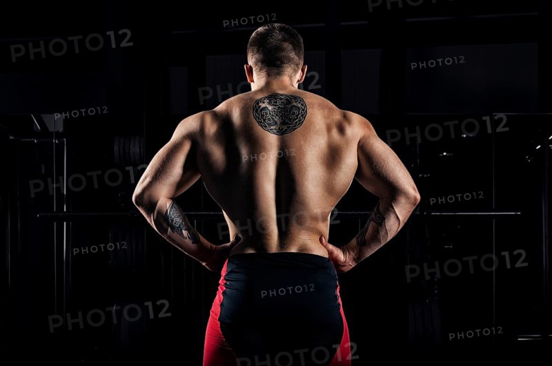 Huge weightlifter stands with his back to the camera and shows his huge back. Back view