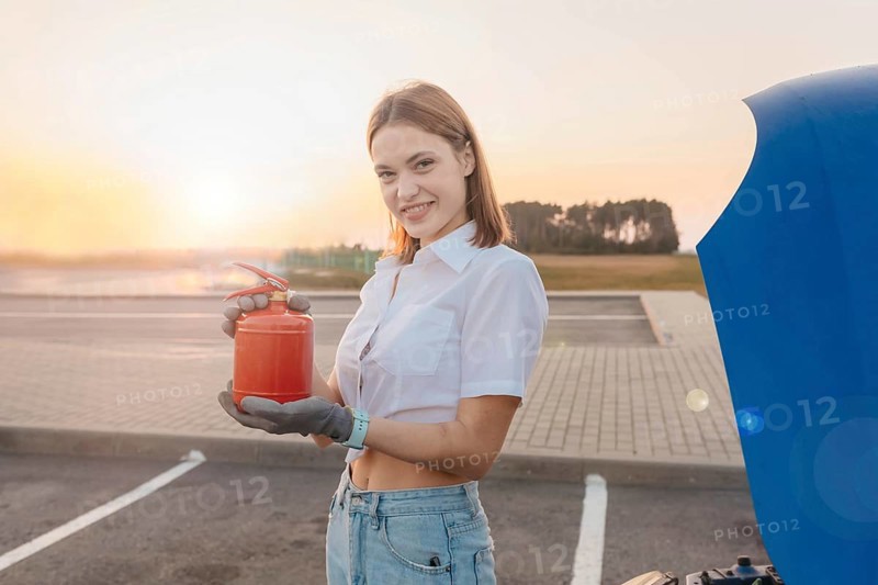 Young beautiful and hot woman driver holds a fire extinguisher in her hands