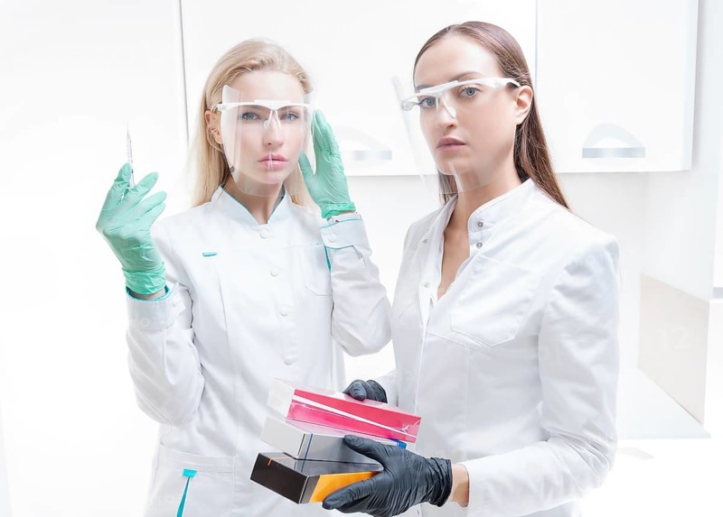 Two beauticians pose in a medical office with cosmetic preparations and a syringe. Skin rejuvenation concept.