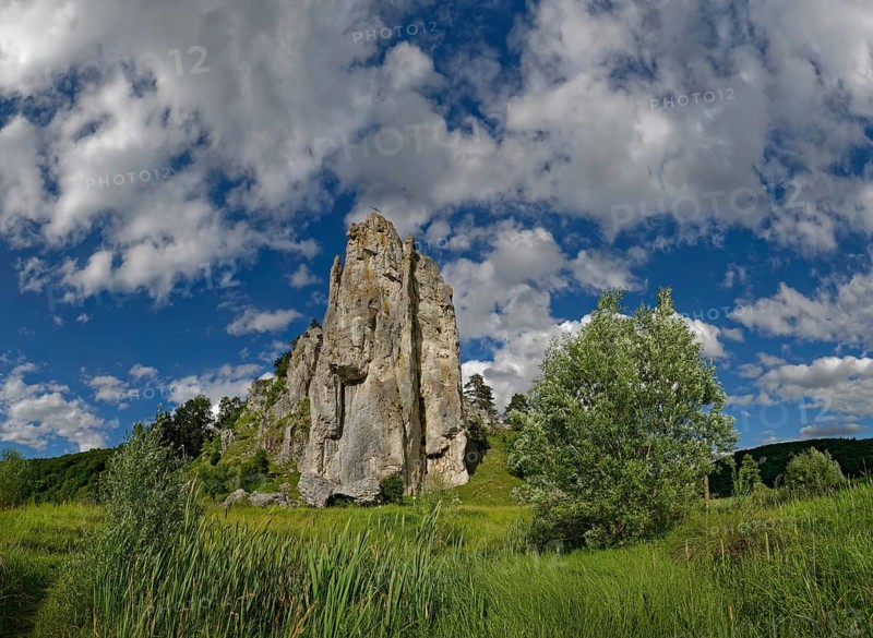 Striking limestone rock formation Burgstein with blue and white sky in the upper Altmuehltal surrounded by green vegetation