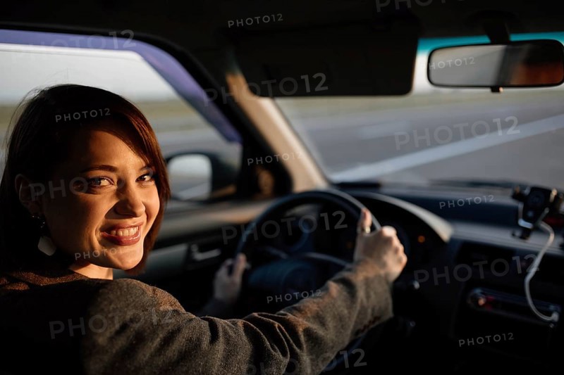 Young beautiful smiling female taxi driver in a jacket greets passengers in a friendly manner