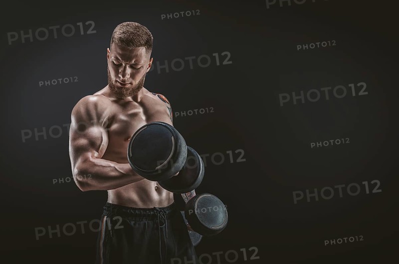 Young muscular guy pumping biceps with dumbbells. Concentrated flexion. Fitness and nutrition concept.